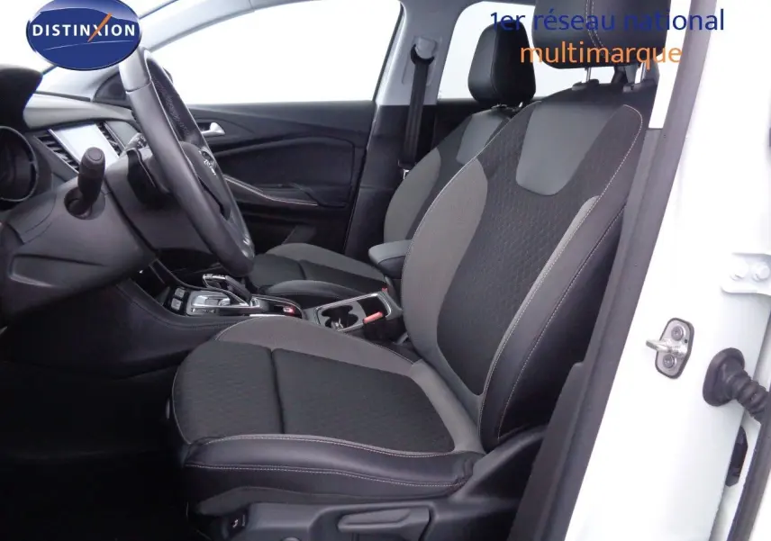 Vue intérieure côté conducteur de l’Opel Grandland X blanc métal, sièges bi-matière noir et gris avec console centrale visible.