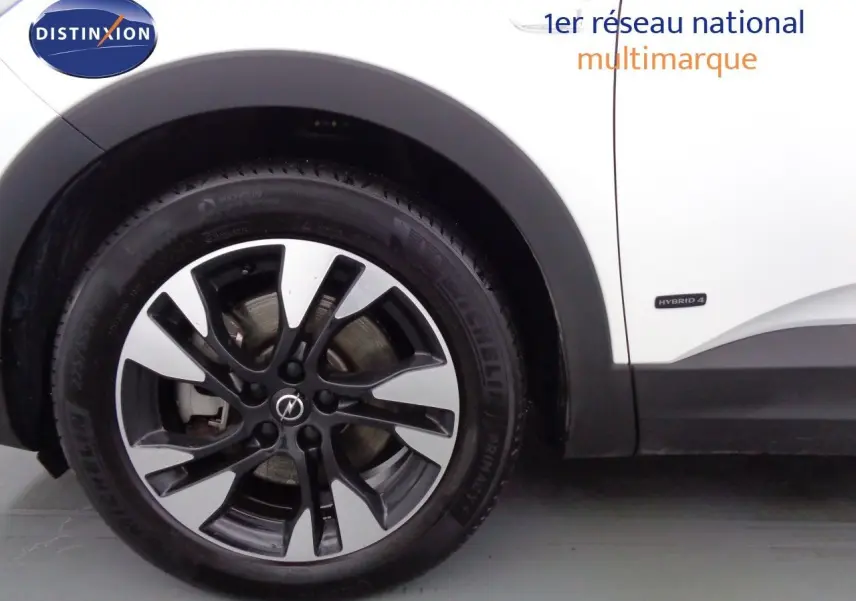 Gros plan sur la roue avant gauche d’un Opel Grandland X blanc métal avec badge Hybrid 4 visible sur la carrosserie.