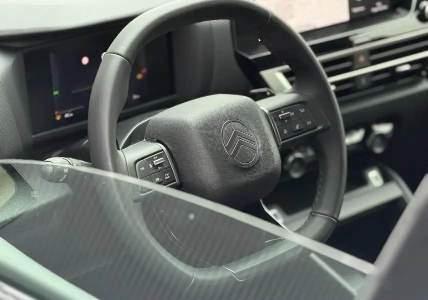 Vue rapprochée du volant cuir noir de la Citroën C4 2025, avec commandes intégrées et tableau de bord numérique en arrière-plan.