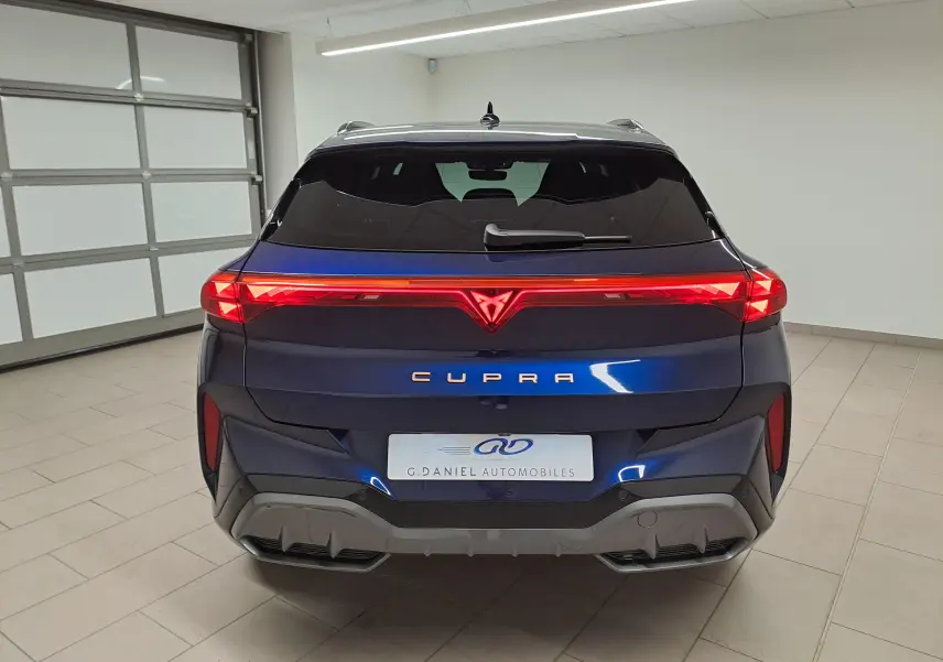 Vue arrière d'une CUPRA TERRAMAR 2025 bleu cosmos avec feux LED reliés et toit ouvrant panoramique visible en intérieur showroom.