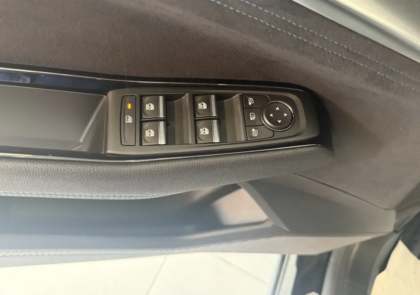 Gros plan sur les commandes de lève-vitres et rétroviseurs côté gauche, garniture noire avec surpiqûres bleues.