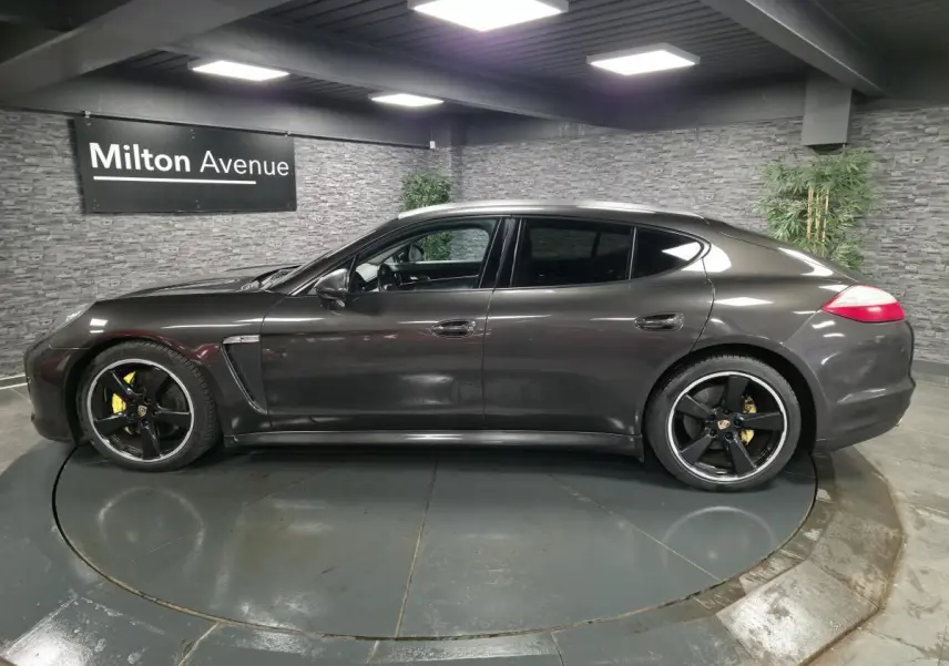 Vue de profil côté gauche d'une Porsche Panamera marron métallisée avec jantes noires sport 20 pouces dans un showroom.