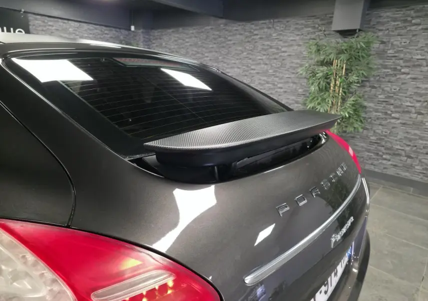 Vue arrière 3/4 droite d'une Porsche Panamera marron avec aileron télescopique déployé et feux arrière rouges.