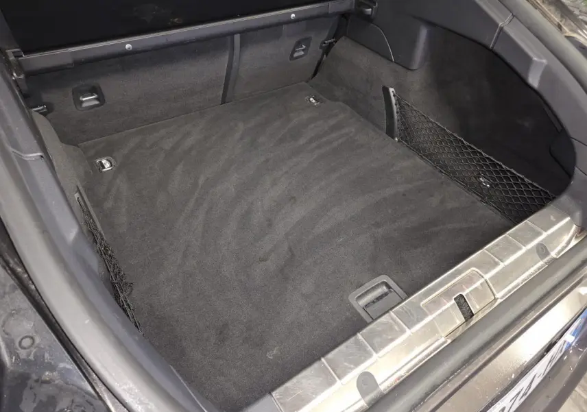 Coffre arrière ouvert de la Porsche Panamera marron, avec tapis noir et filets de rangement latéraux.