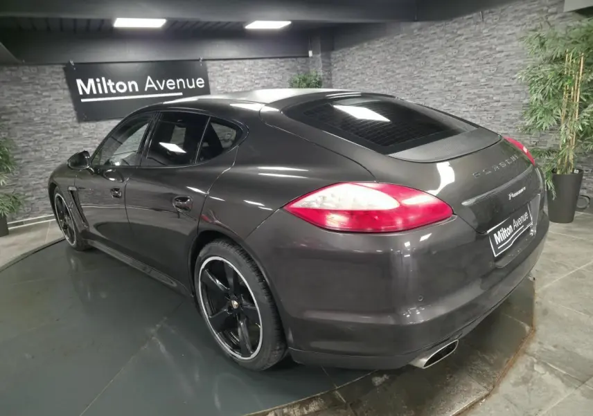 Vue 3/4 arrière droite d'une Porsche Panamera marron métallisée avec jantes noires 20 pouces et sorties d'échappement doubles.