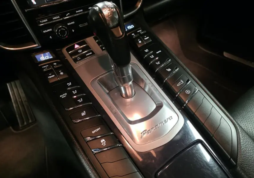 Gros plan sur la console centrale intérieure noire de la Porsche Panamera marron, avec levier de vitesse et commandes sport visibles.