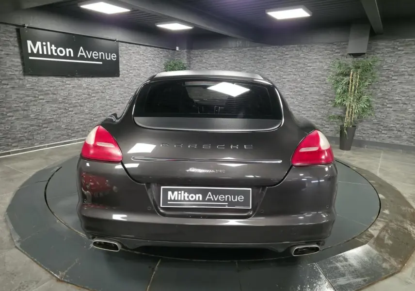 Vue arrière d'une Porsche Panamera marron métallisé avec double sortie d'échappement et hayon chromé dans un showroom.