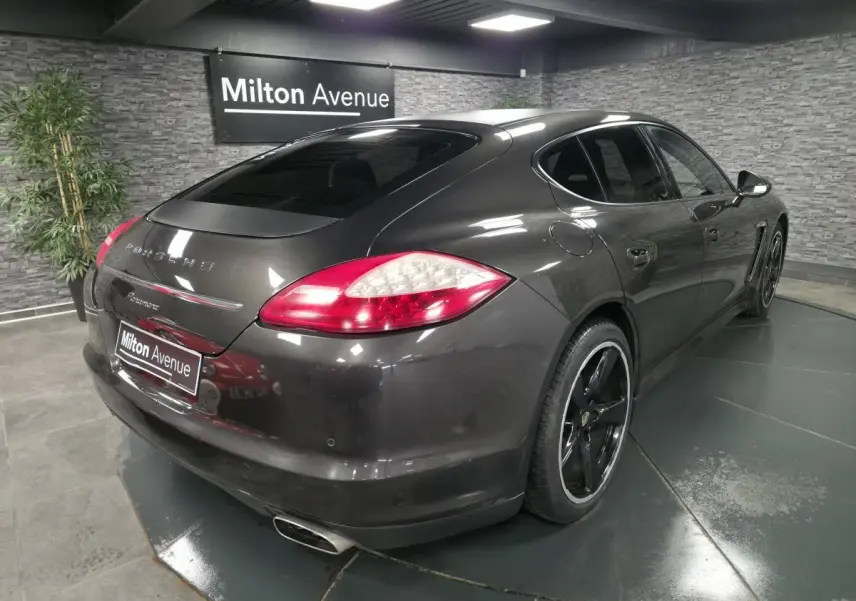 Vue 3/4 arrière droite d'une Porsche Panamera marron métallisée avec jantes noires sport et double sortie d'échappement.