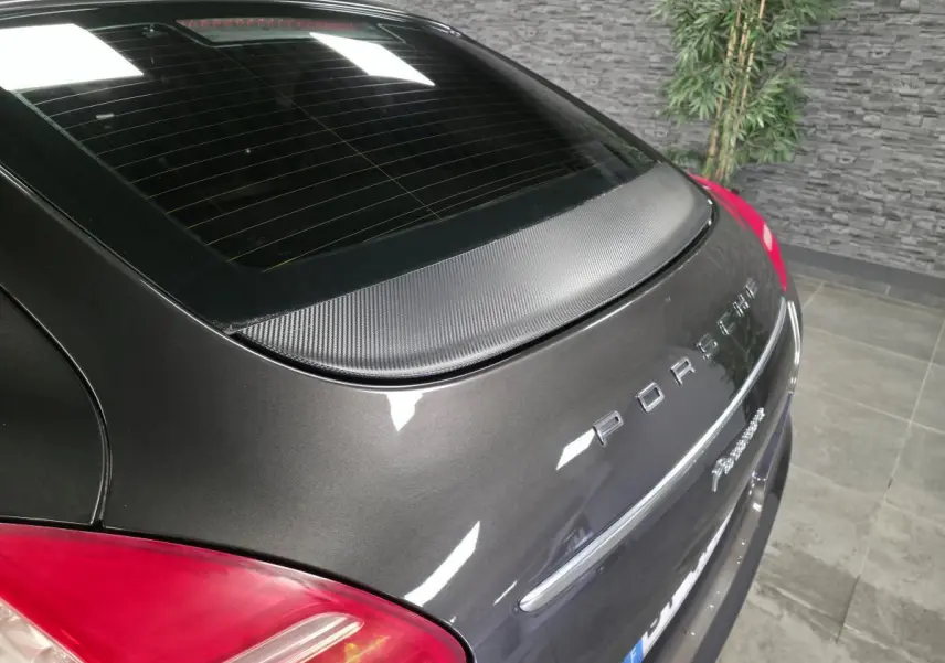 Vue arrière en léger angle droit d'une Porsche Panamera marron métallisée avec aileron carbone et feux rouges.