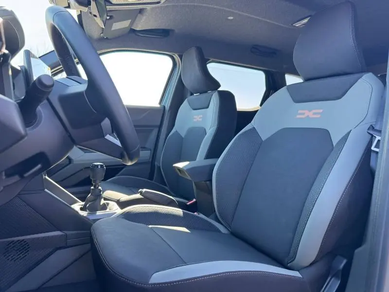 Vue intérieure côté gauche du Dacia Duster 2025, sièges tissu noir et gris avec logo DC brodé, volant multifonction visible.