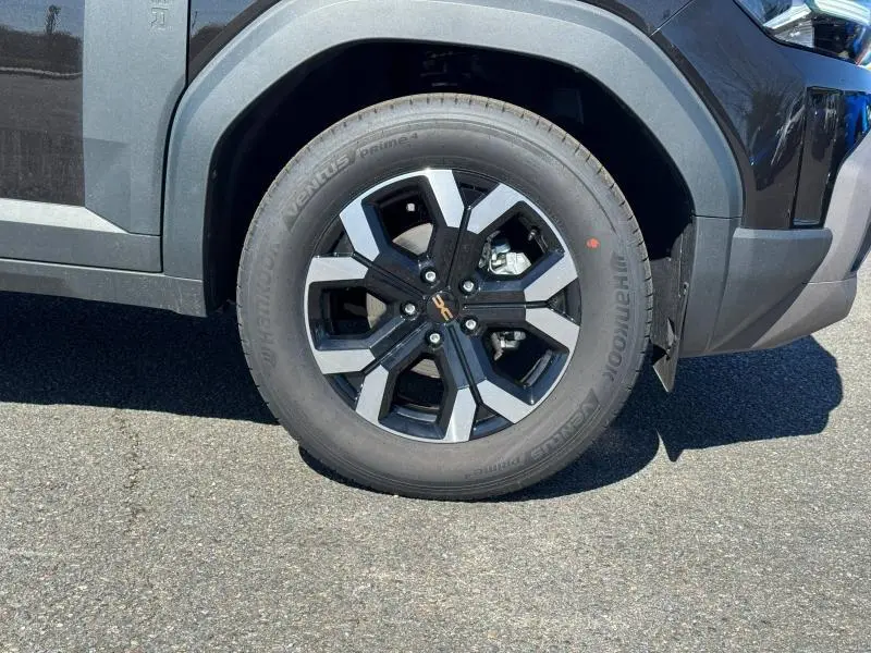 Gros plan sur la roue avant droite du Dacia Duster 2025, jante alu noire et grise avec logo Dacia au centre.