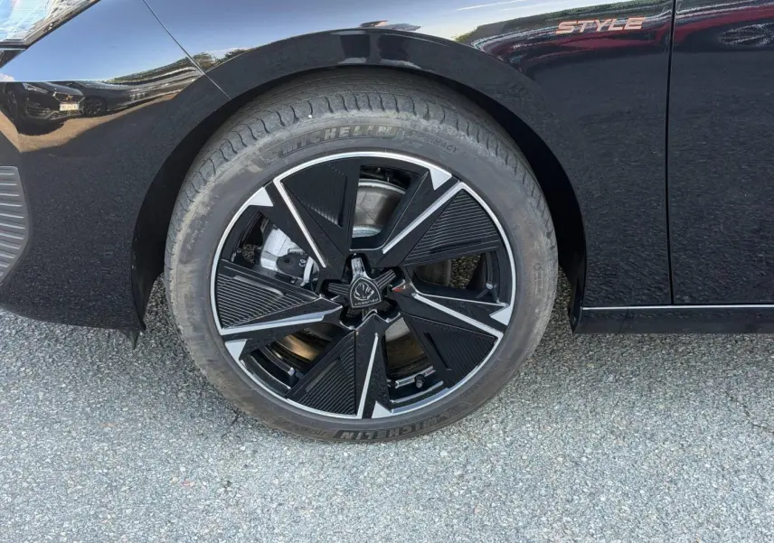 Gros plan sur la roue avant gauche noire avec jante alu design et logo Peugeot, sur carrosserie noire Perla Nera Style.