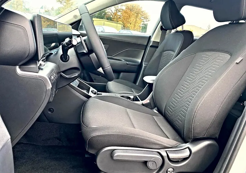 Vue intérieure côté conducteur du Hyundai Kona 2025 gris, avec sièges tissu et volant multifonction cuir.