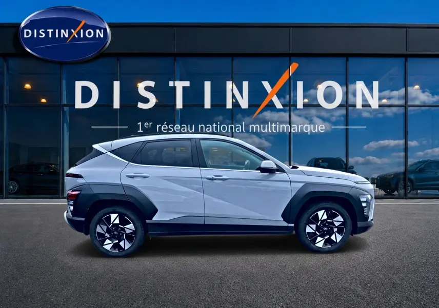 Vue latérale droite d'un Hyundai Kona gris 2025 avec protections noires et jantes alliage distinctives devant une vitrine Distinxion.