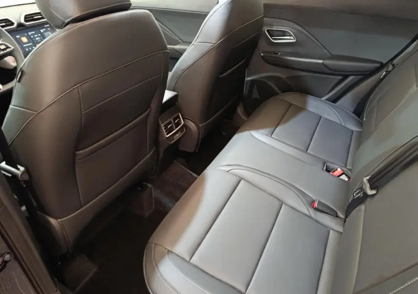 Vue intérieure arrière du MG Motor ZS 1.5L Hybrid+ Luxury 2026, sièges en cuir gris foncé avec accoudoir central.