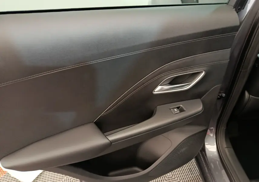 Gros plan sur la porte intérieure côté droit du MG Motor ZS gris foncé, avec poignée argentée et bouton de vitre électrique.
