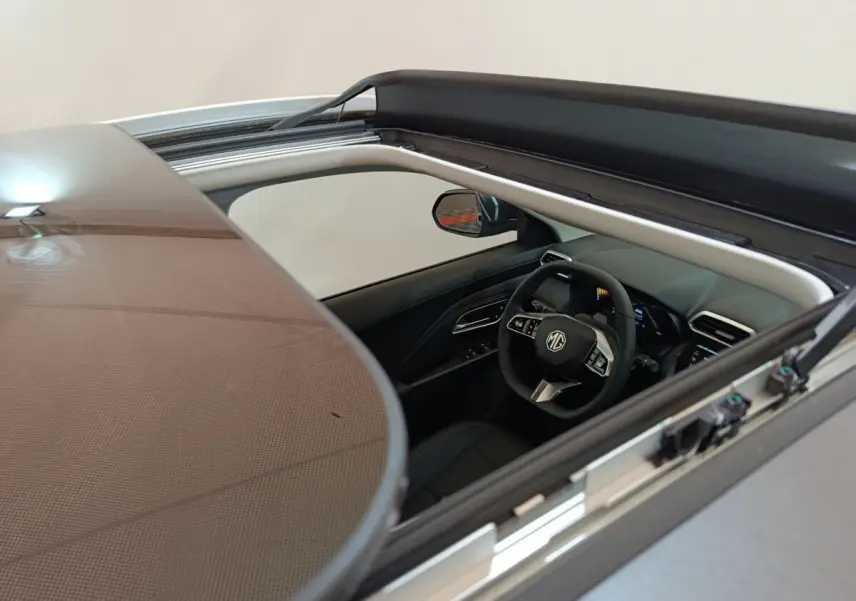Vue intérieure par le toit ouvrant du MG ZS gris foncé, mettant en valeur le volant multifonctions et le tableau de bord moderne.