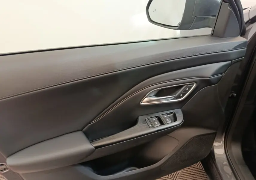 Vue intérieure côté gauche de la porte avant gris foncé du MG ZS 1.5L Hybrid+ Luxury avec commandes de vitres et poignée argentée.