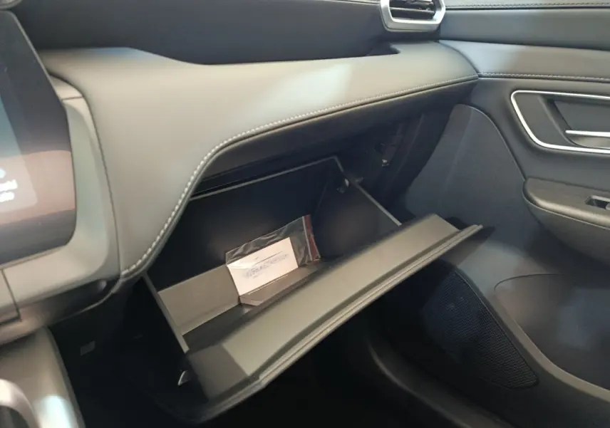 Intérieur MG ZS 2026, vue côté passager sur boîte à gants ouverte avec tableau de bord gris foncé et coutures apparentes.