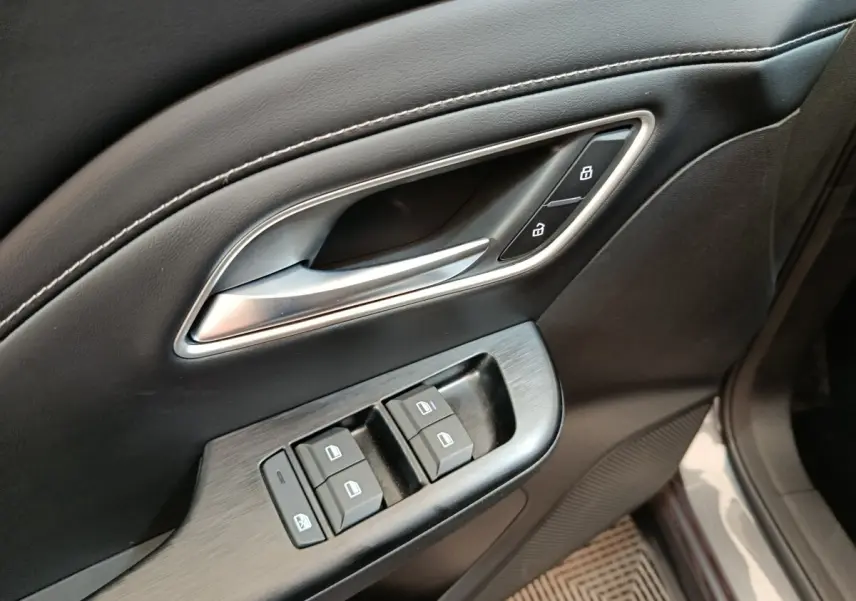Gros plan sur la commande des vitres et la poignée de porte intérieure en cuir noir du MG MOTOR ZS gris foncé.