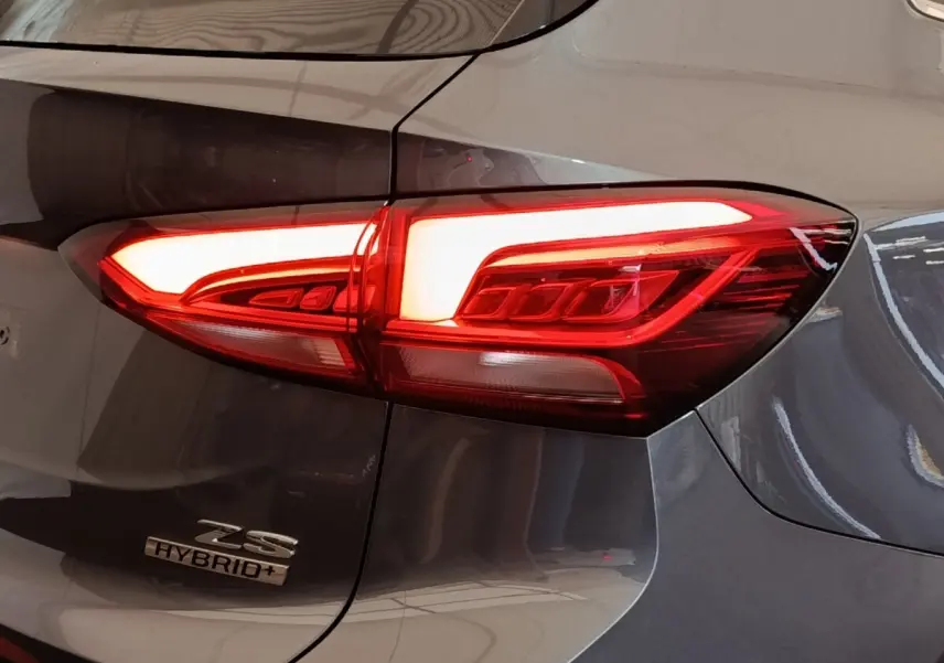 Gros plan sur le feu arrière droit allumé d’un MG ZS Hybrid+ gris foncé avec logo et détails de carrosserie visibles.