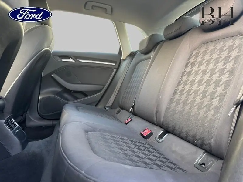 Vue intérieure de la banquette arrière en tissu noir avec motifs pied-de-poule, sièges et ceintures visibles côté droit.