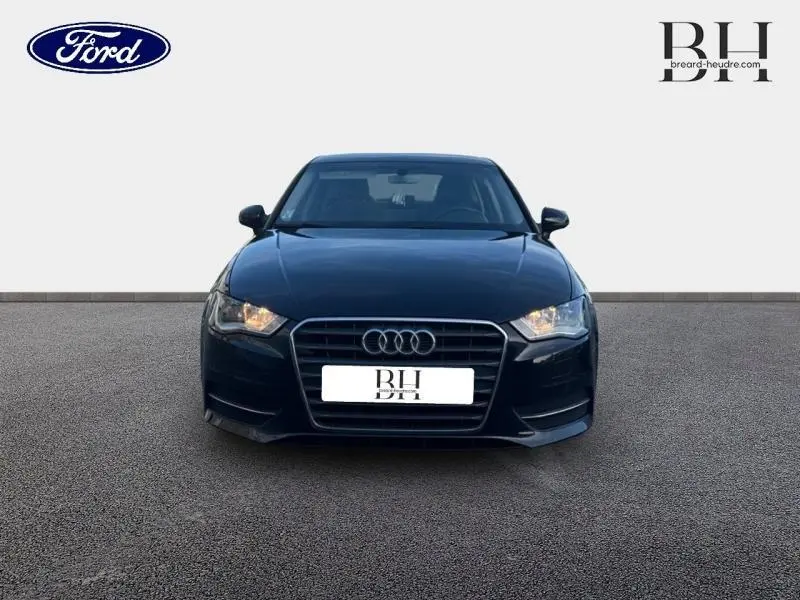 Vue frontale d'une Audi A3 Sportback noire brillante avec phares allumés et calandre distinctive aux anneaux Audi.