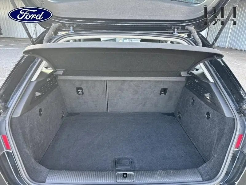 Coffre ouvert vu de l'arrière d'une Audi A3 Sportback noire brillante, montrant l'espace de chargement et la tablette cache-bagages.