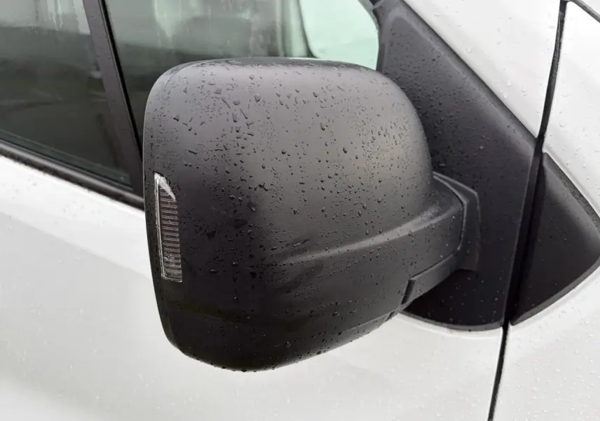 Rétroviseur droit noir avec clignotant intégré sur Renault Trafic blanc glacier sous la pluie.