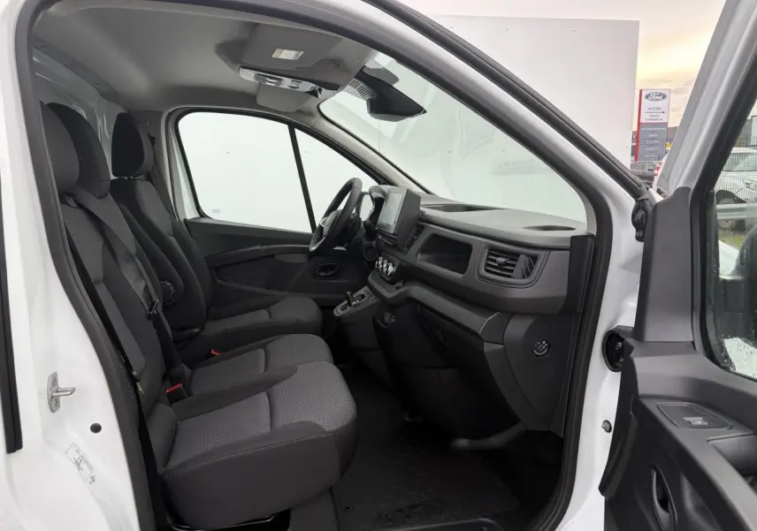 Vue intérieure côté conducteur du Renault Trafic Fourgon blanc glacier, montrant les sièges tissu Kompo et le tableau de bord avec écran tactile.