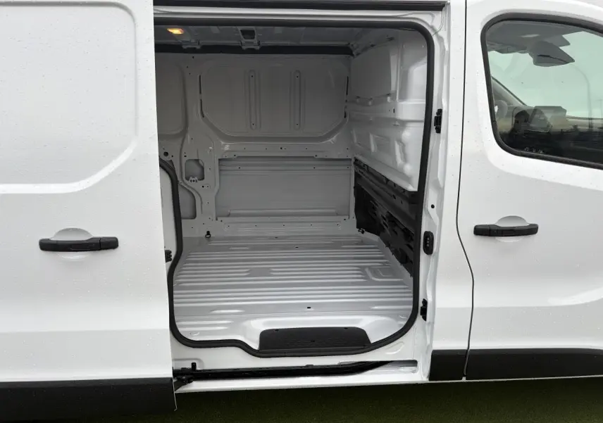 Vue latérale gauche du Renault Trafic Fourgon blanc glacier avec porte coulissante ouverte dévoilant l’espace de chargement vide.
