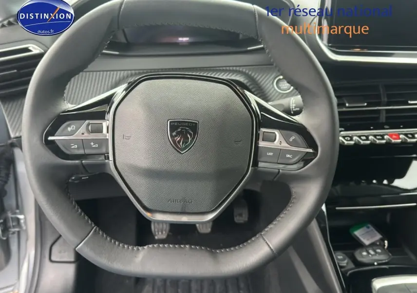 Vue rapprochée du volant cuir noir de la Peugeot 208 2024 avec commandes intégrées et logo central.