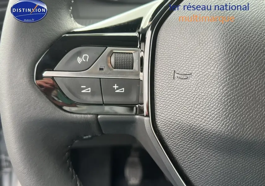 Gros plan sur les commandes de volume au volant noir de la Peugeot 208 1.2 PureTech 100 Allure 2024.