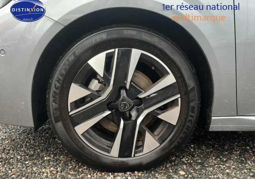 Gros plan sur la roue avant gauche d'une Peugeot 208 gris artense avec jante alu au design moderne.