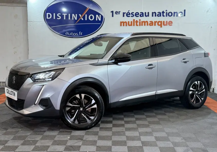 Peugeot 2008 gris clair en vue 3/4 avant droit, avec jantes noires et toit noir contrasté en intérieur showroom.