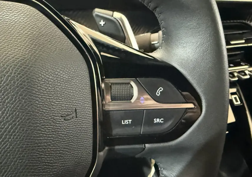 Gros plan sur les commandes gauche du volant en cuir noir du Peugeot 2008 gris clair, avec boutons multifonctions visibles.