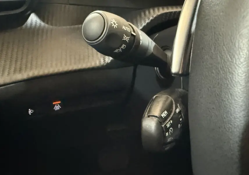 Gros plan sur les commandes au volant du Peugeot 2008 gris clair, avec levier d'éclairage et régulateur de vitesse.