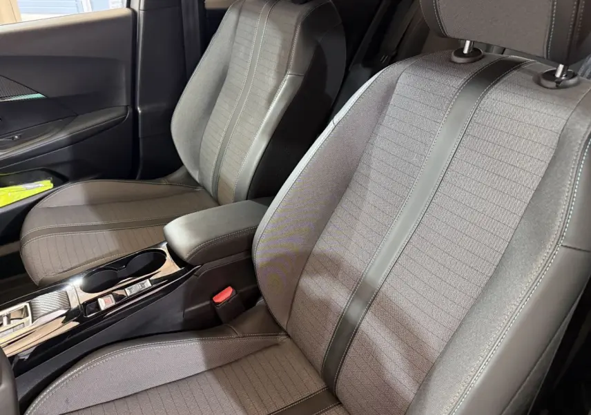 Vue rapprochée des sièges avant gris clair et tissu avec surpiqûres, console centrale noire brillante d’une Peugeot 2008 2023.