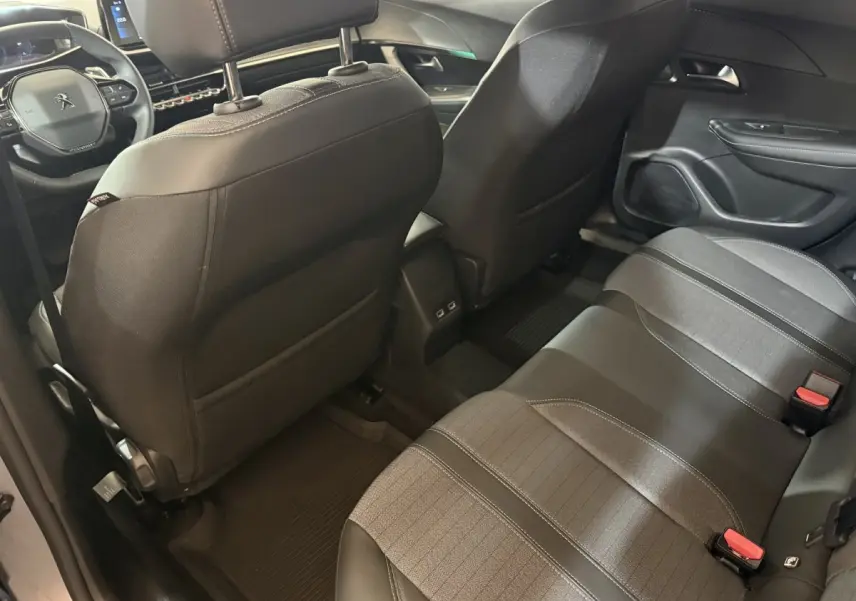 Vue intérieure arrière du Peugeot 2008 gris clair 2023, montrant les sièges tissu et cuir et le tableau de bord avant.