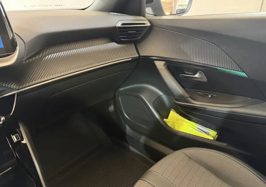 Vue intérieure côté passager avant du Peugeot 2008 gris clair, avec tableau de bord à effet carbone et porte avec rangement.