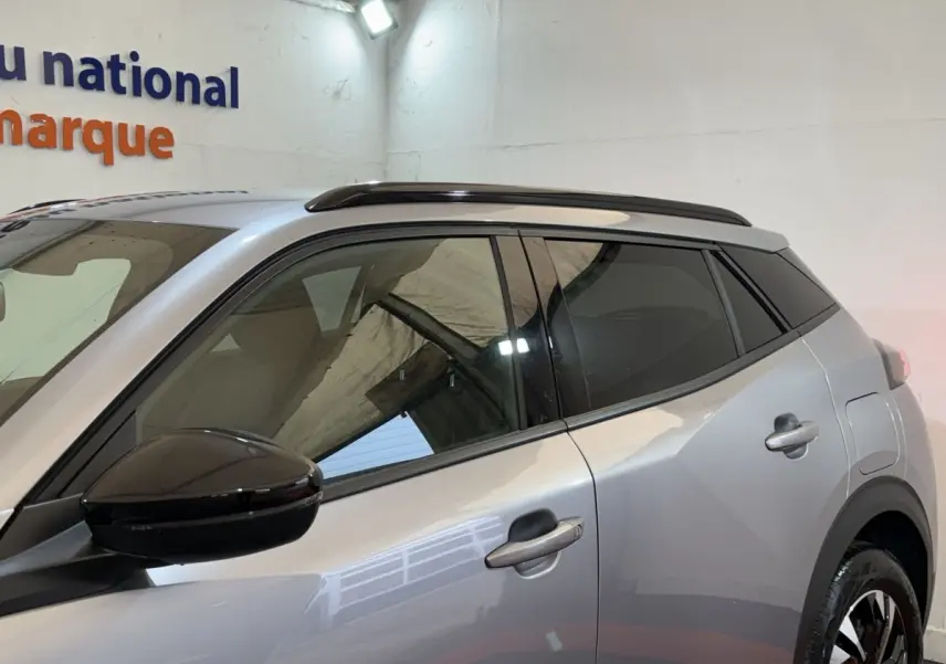 Vue latérale droite du Peugeot 2008 gris clair 2023 avec rétroviseur noir et toit ouvrant panoramique.