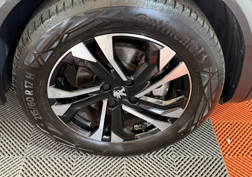 Gros plan sur la roue avant droite du Peugeot 2008 gris clair, jante alliage noire et argentée avec logo lion central.