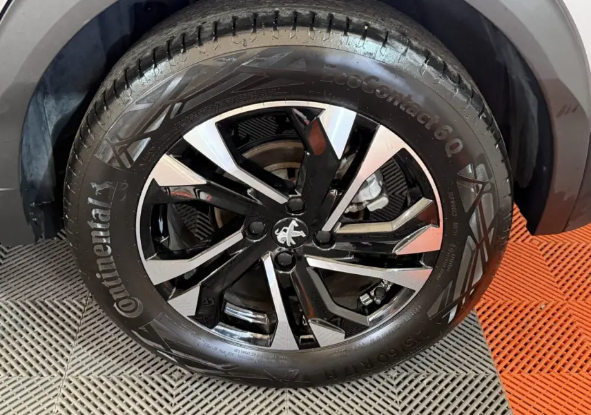 Gros plan sur la roue avant droite du Peugeot 2008 gris clair, jante alliage noire et argentée au design moderne.