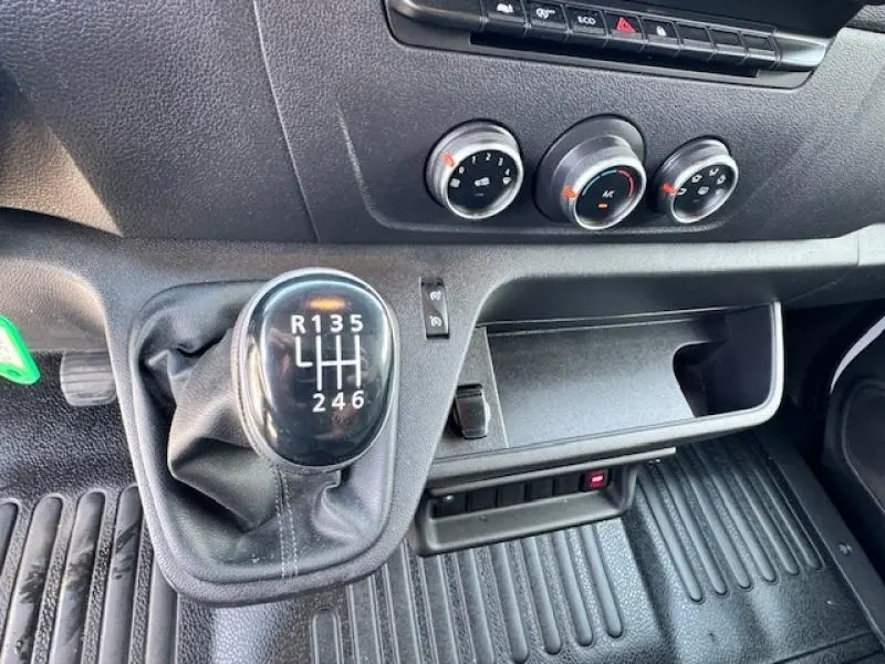 Gros plan intérieur sur le levier de vitesses manuel et les commandes de climatisation du Renault Master Combi blanc.