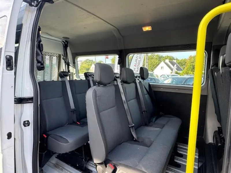 Vue intérieure côté gauche du Renault Master Combi blanc minéral, montrant les sièges gris en rangées avec ceintures de sécurité.