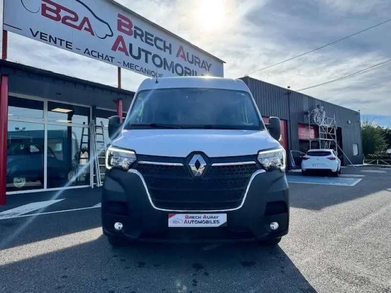 Vue de face d'un Renault Master Combi blanc minéral stationné devant un garage avec calandre noire et phares allumés.
