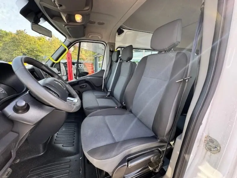 Vue intérieure côté conducteur du Renault Master Combi blanc, montrant les sièges avant en tissu gris foncé et le volant.