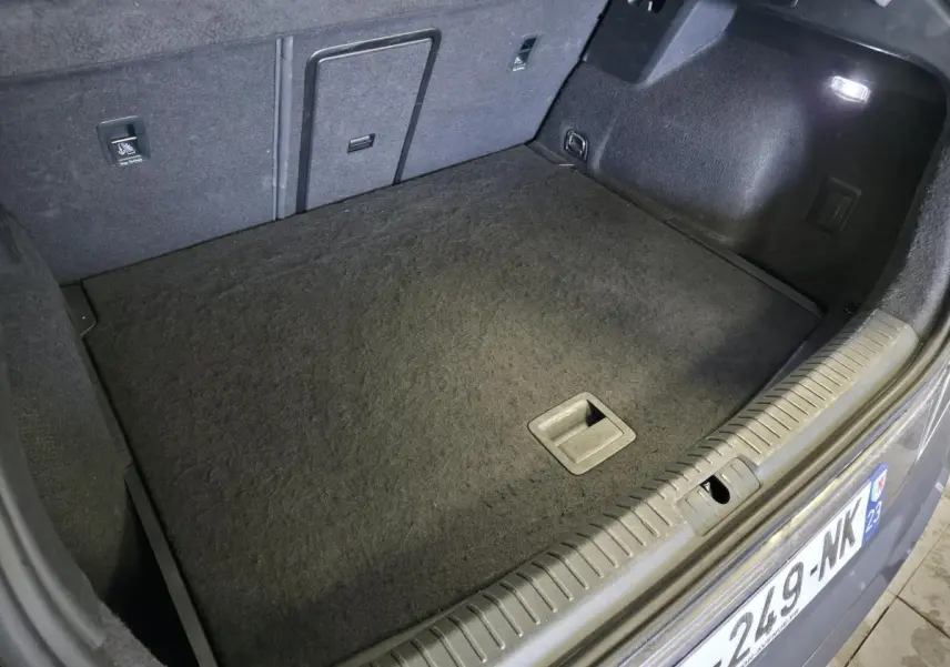 Coffre ouvert du CUPRA Formentor bleu, vue plongeante sur le tapis de sol et hayon électrique avec éclairage intérieur.