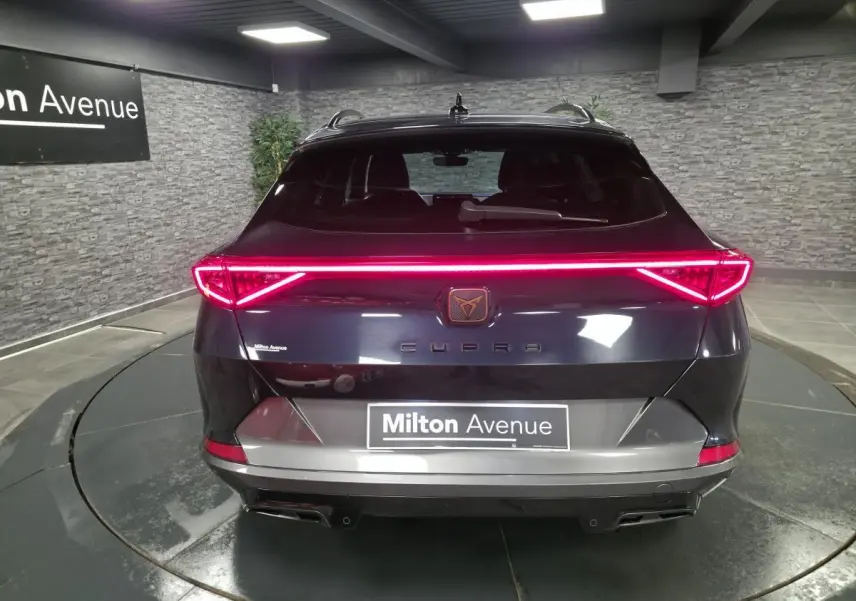 Vue arrière d'un CUPRA Formentor bleu avec bandeau lumineux LED et double sortie d'échappement noire dans un showroom.
