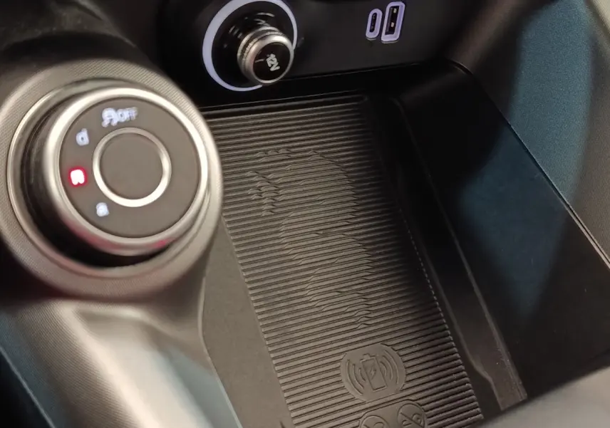 Gros plan sur la console centrale de l'Alfa Romeo Tonale bleu, montrant la molette de sélection et la zone de recharge sans fil.